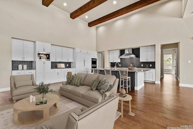 living area with baseboards, beam ceiling, recessed lighting, a towering ceiling, and wood finished floors