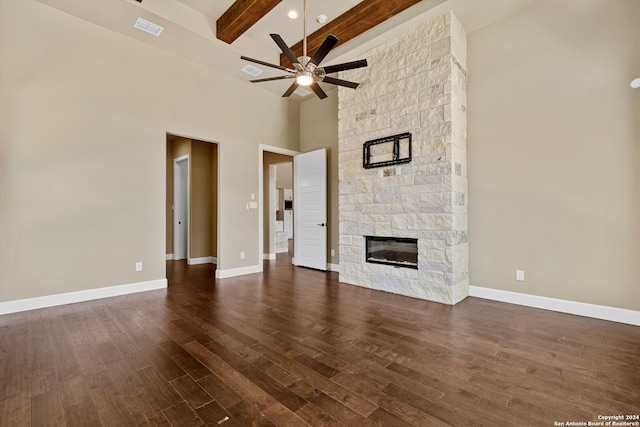 unfurnished living room with a stone fireplace, beam ceiling, dark wood-type flooring, high vaulted ceiling, and ceiling fan