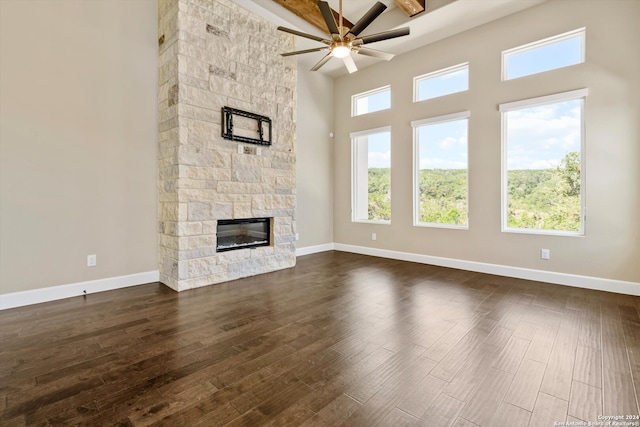 unfurnished living room with ceiling fan, a towering ceiling, dark hardwood / wood-style flooring, and a fireplace