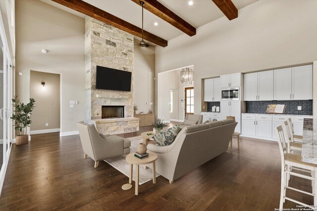 living room with a notable chandelier, a stone fireplace, a towering ceiling, dark wood-type flooring, and beam ceiling