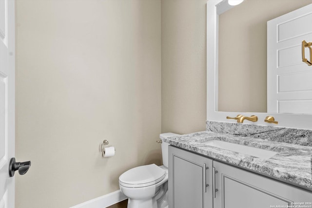 half bath featuring baseboards, toilet, and vanity