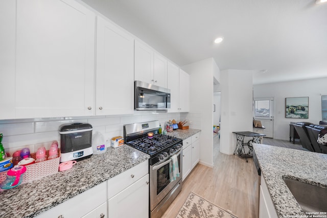 kitchen with appliances with stainless steel finishes, light stone counters, light hardwood / wood-style floors, and tasteful backsplash