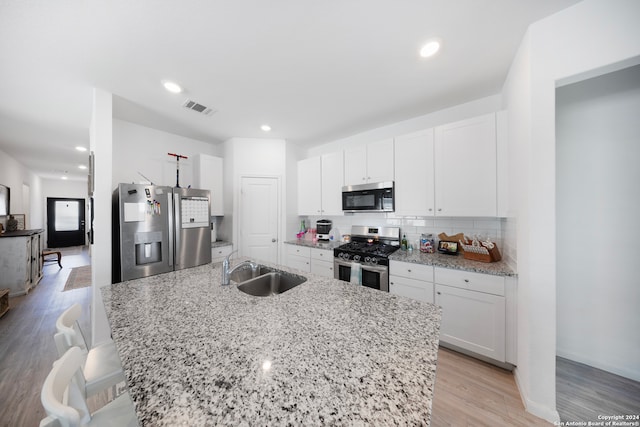 kitchen featuring appliances with stainless steel finishes, light hardwood / wood-style floors, white cabinetry, sink, and decorative backsplash