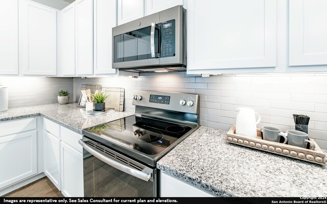 kitchen with appliances with stainless steel finishes, dark hardwood / wood-style flooring, light stone counters, and white cabinets