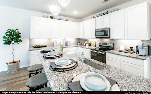 kitchen with hardwood / wood-style floors, stainless steel appliances, white cabinetry, sink, and a kitchen breakfast bar