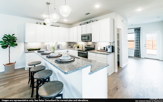 kitchen featuring light wood-type flooring, appliances with stainless steel finishes, white cabinetry, a kitchen breakfast bar, and a kitchen island