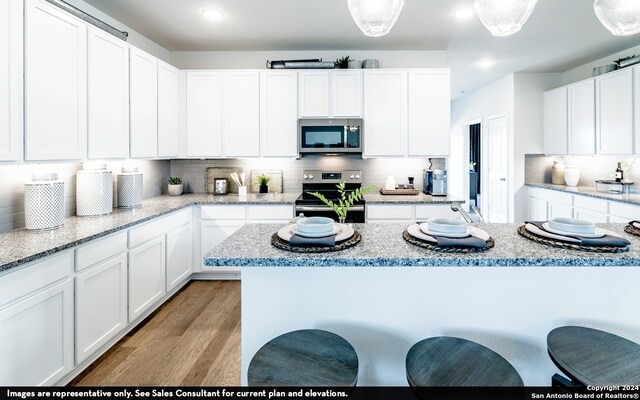 kitchen with decorative light fixtures, appliances with stainless steel finishes, light wood-type flooring, and white cabinetry