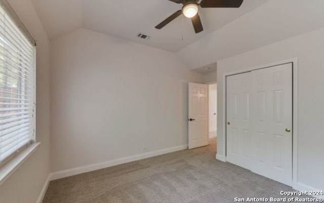 unfurnished bedroom with lofted ceiling, a closet, ceiling fan, and light carpet