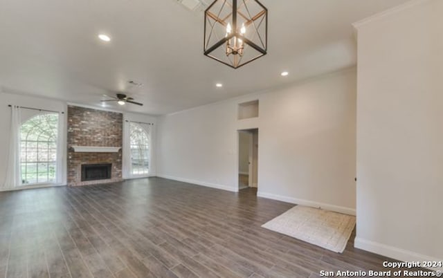 unfurnished living room featuring dark wood-type flooring, ornamental molding, ceiling fan with notable chandelier, and a fireplace