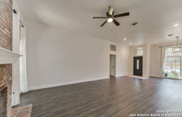 unfurnished living room with a fireplace, ceiling fan with notable chandelier, a barn door, and dark hardwood / wood-style floors