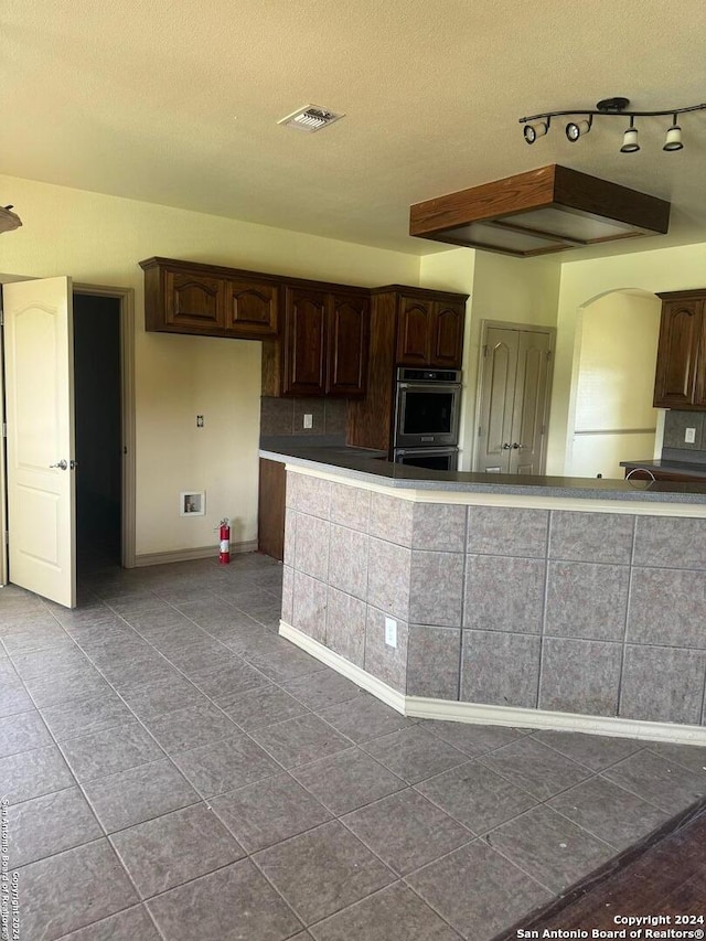 kitchen featuring light tile patterned floors, a textured ceiling, dark brown cabinets, and stainless steel double oven