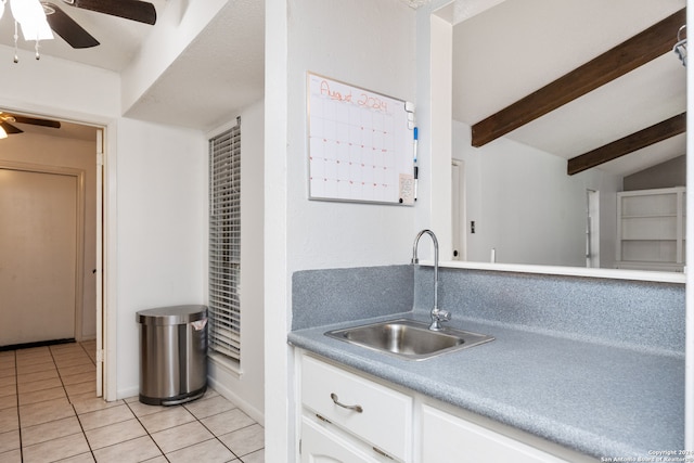 kitchen featuring light tile patterned floors, white cabinetry, sink, ceiling fan, and vaulted ceiling with beams