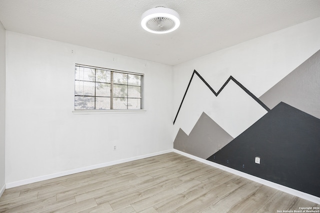 empty room with a textured ceiling and light hardwood / wood-style flooring