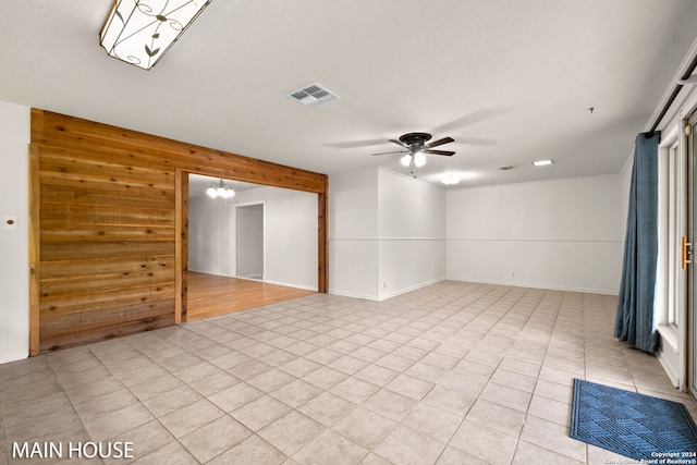 unfurnished room with ceiling fan with notable chandelier, wooden walls, and a textured ceiling