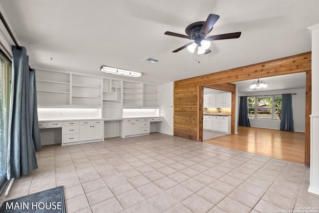 interior space with built in desk, ceiling fan with notable chandelier, white cabinetry, a textured ceiling, and light tile patterned flooring