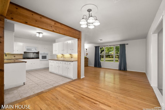 kitchen with white appliances, backsplash, light hardwood / wood-style floors, a chandelier, and white cabinets