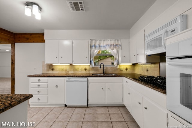 kitchen with dark stone counters, white cabinetry, white appliances, tasteful backsplash, and sink