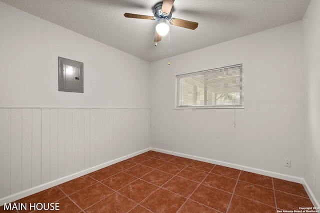 spare room featuring electric panel, ceiling fan, dark tile patterned flooring, and a textured ceiling