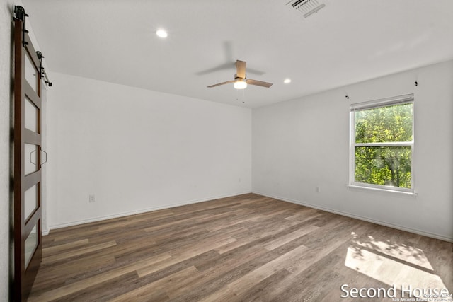 spare room featuring a barn door, ceiling fan, and wood-type flooring