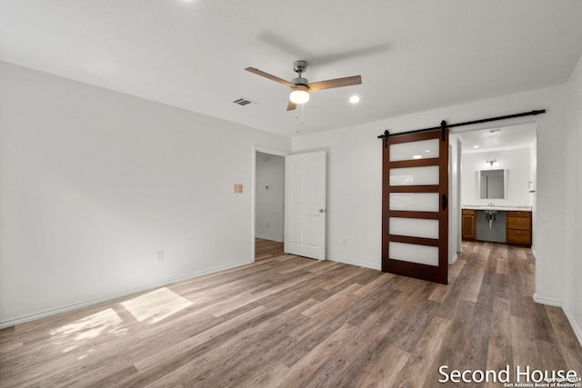 unfurnished bedroom with a barn door, hardwood / wood-style floors, ceiling fan, and ensuite bathroom