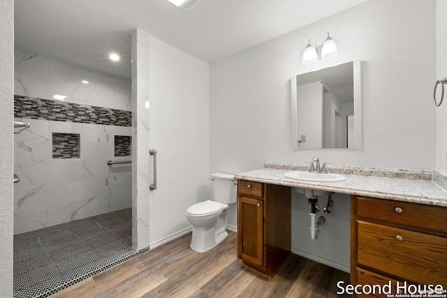 bathroom featuring toilet, sink, wood-type flooring, tiled shower, and a textured ceiling