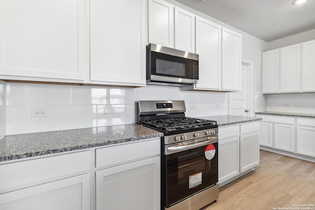 kitchen featuring stone countertops, white cabinetry, stainless steel appliances, and backsplash