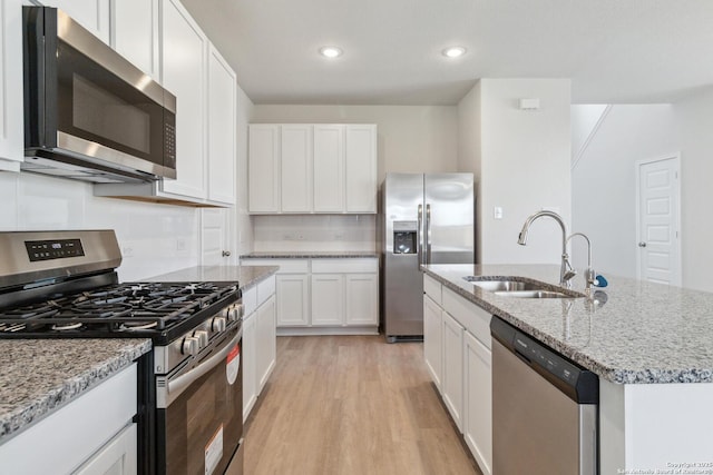 kitchen with a kitchen island with sink, stainless steel appliances, a sink, white cabinetry, and light wood finished floors