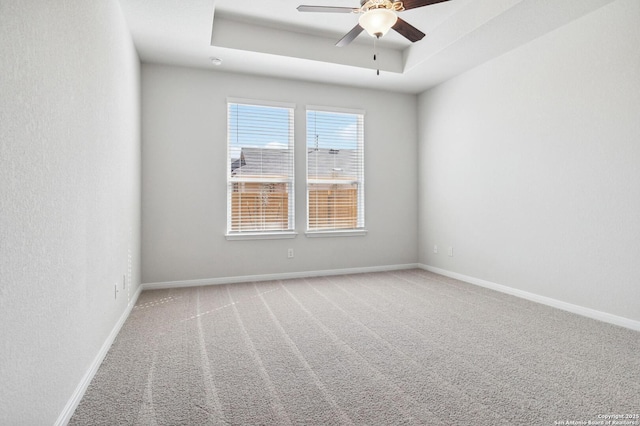 carpeted spare room featuring a ceiling fan, a tray ceiling, and baseboards