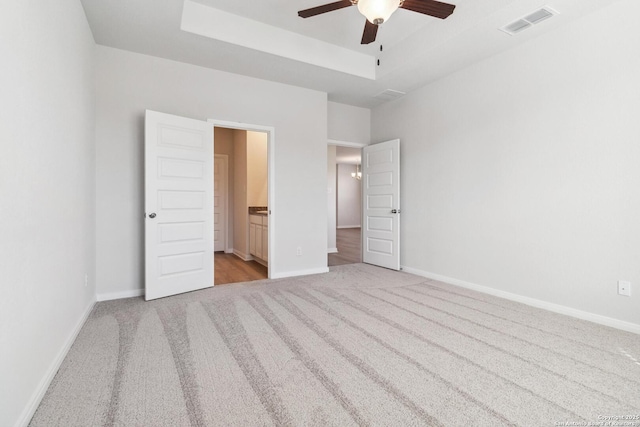 unfurnished bedroom featuring baseboards, visible vents, a raised ceiling, and light colored carpet