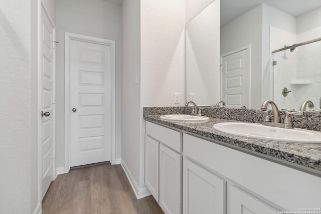 bathroom with double vanity, wood finished floors, tiled shower, and a sink