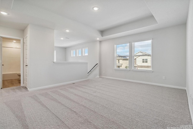 carpeted spare room featuring baseboards, a raised ceiling, and recessed lighting