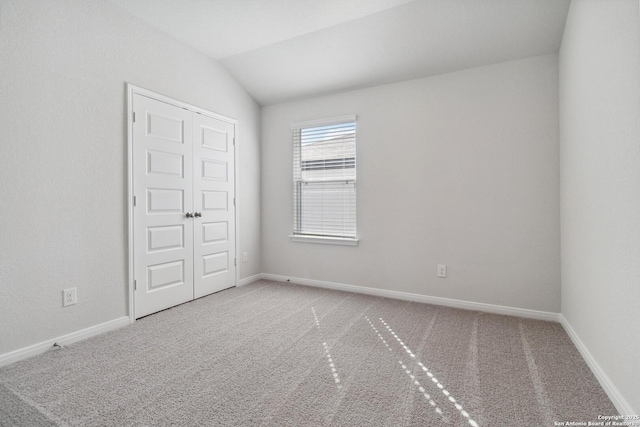 carpeted empty room featuring baseboards and vaulted ceiling