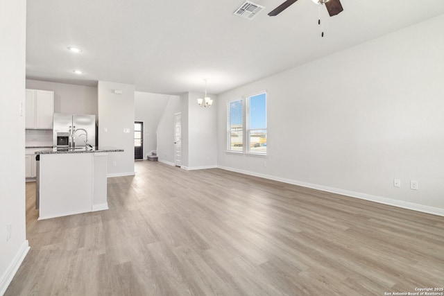 unfurnished living room featuring visible vents, baseboards, light wood-style flooring, ceiling fan with notable chandelier, and recessed lighting