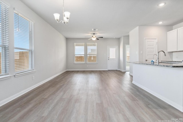 unfurnished living room with visible vents, a sink, light wood-type flooring, baseboards, and ceiling fan with notable chandelier