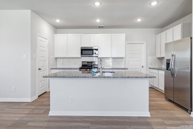 kitchen with stainless steel appliances, visible vents, light wood-style floors, white cabinets, and dark stone countertops