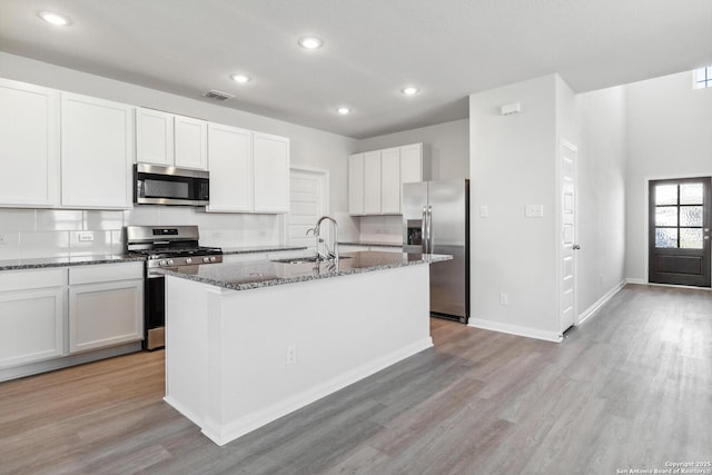 kitchen with stainless steel appliances, a sink, visible vents, light wood-type flooring, and dark stone counters