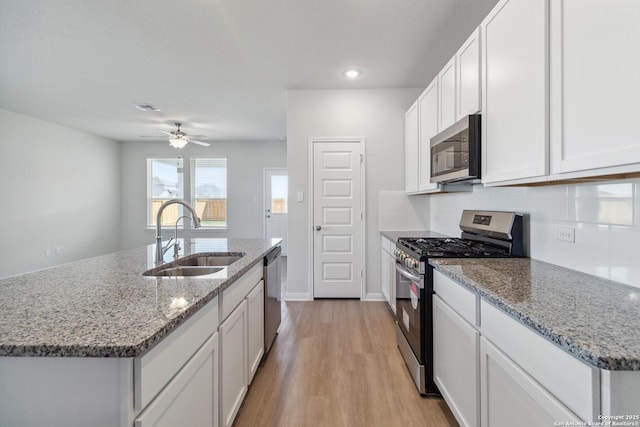 kitchen with appliances with stainless steel finishes, light wood-type flooring, a sink, and light stone countertops