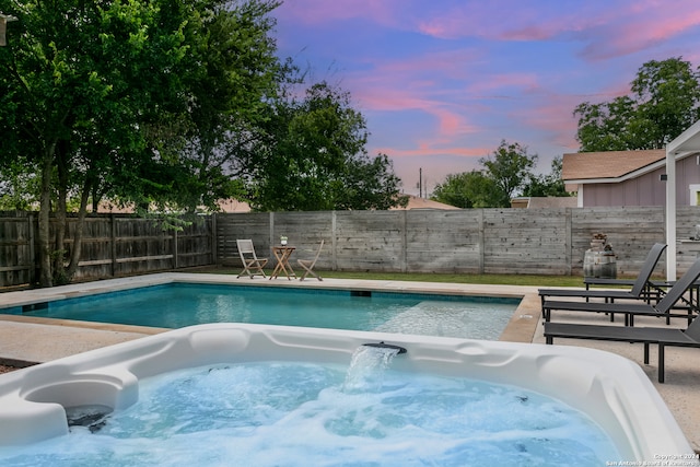 pool at dusk featuring a hot tub