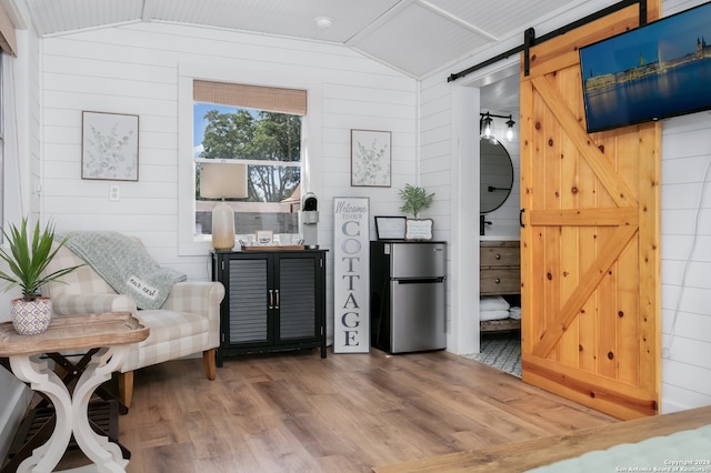 sitting room with a barn door, vaulted ceiling, hardwood / wood-style floors, and wooden walls