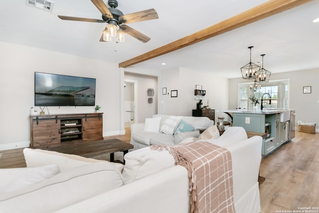 living room with ceiling fan with notable chandelier, beamed ceiling, and light hardwood / wood-style floors