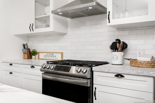 kitchen with backsplash, stainless steel range oven, light stone counters, wall chimney exhaust hood, and white cabinets