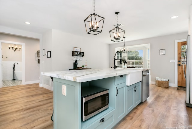 kitchen featuring an inviting chandelier, decorative light fixtures, a center island with sink, light hardwood / wood-style flooring, and sink