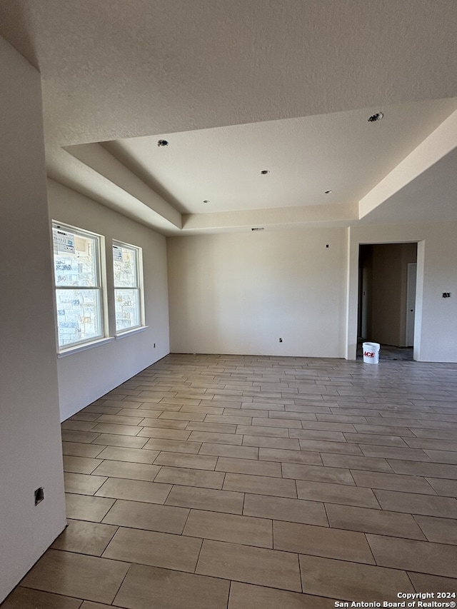 spare room with light hardwood / wood-style flooring, a textured ceiling, and a tray ceiling