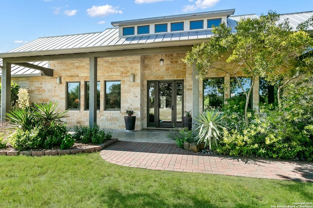 exterior space featuring a lawn, a standing seam roof, stone siding, french doors, and metal roof