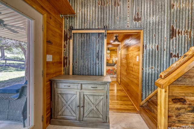 doorway featuring light hardwood / wood-style flooring, ceiling fan, a barn door, and wooden walls