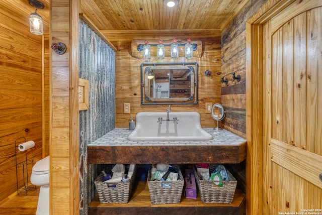 bathroom with toilet, wood walls, sink, and wooden ceiling