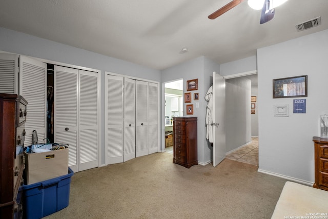 bedroom featuring light colored carpet, two closets, and ceiling fan