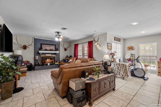 tiled living room featuring ceiling fan, a textured ceiling, and a brick fireplace