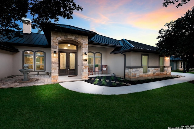 view of front of home with a standing seam roof, stucco siding, french doors, stone siding, and metal roof