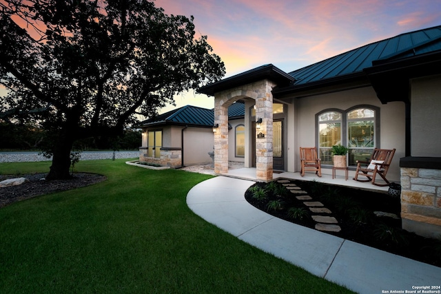 view of front facade featuring stucco siding, a lawn, a standing seam roof, stone siding, and metal roof